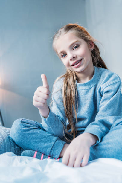istock smiling little girl showing thumb up sign while sitting on bed 690859242