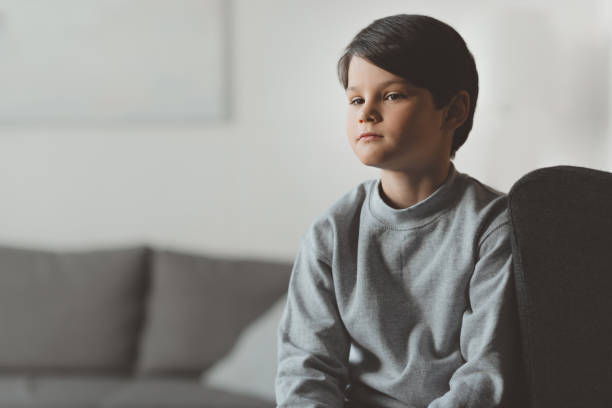 istock pensive little kid boy sitting on sofa at home 690859654