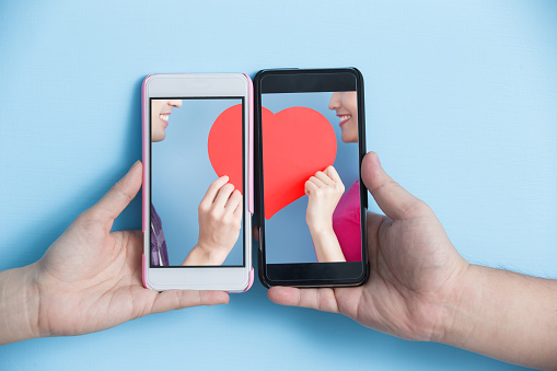 hand take smart phone with young couple take heart in screen on blue background