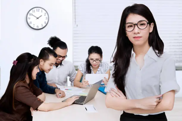 Portrait of a young female entrepreneur standing in front of her team and folded hand, shot in a business meeting