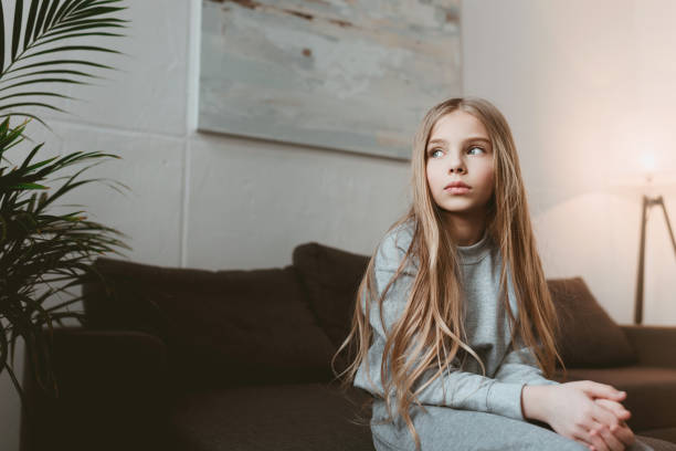 istock little pensive kid girl sitting on sofa alone 690870918