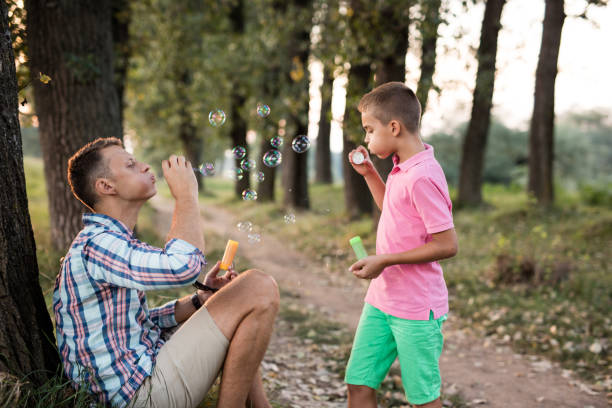 istock Cute kid and his father blowing soap bubbles at the countryside 690871772