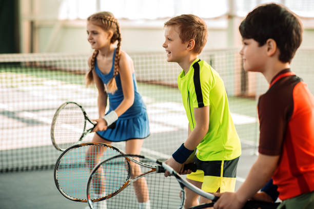 Happy girl and boys playing tennis stock photo