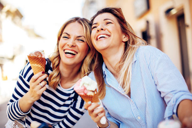 istock Two young women laughing and holding ice cream in hand 690883334