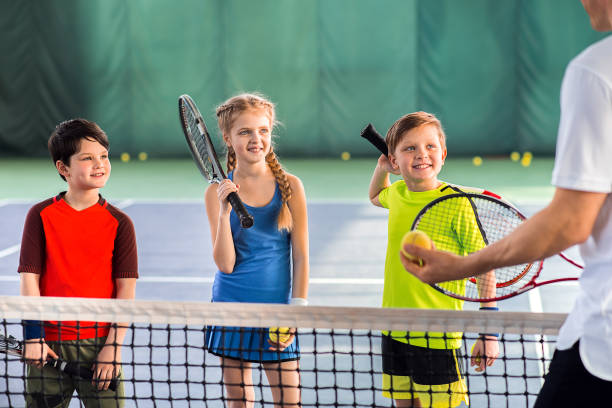 alunni gioiosi che imparano a giocare a tennis - tennis foto e immagini stock