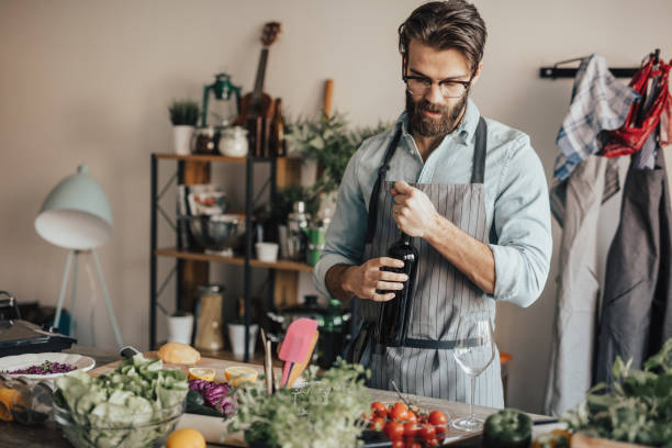 handsome man in kitchen opening a bottle of red wine - wine bottle wine residential structure alcohol imagens e fotografias de stock