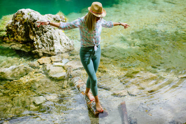 Young girl performs handstand on log on mountain lake, below mountains and forest, Whistler, B.C.