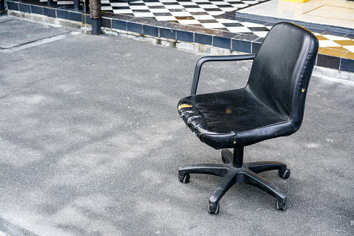 broken dead leather chair on an outdoor concrete floor.