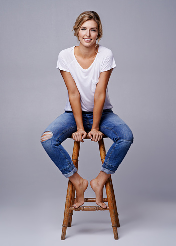 Studio shot of a beautiful young woman posing on a stool against a gray background