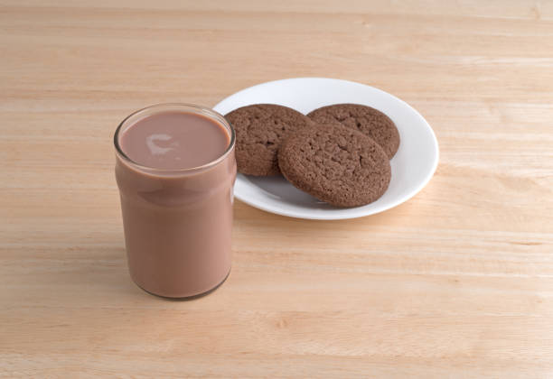 A glass of chocolate milk plus a plate of cookies on a wood table.