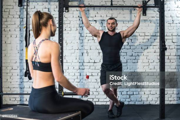 Sportswoman Sitting And Looking At Sportsman Doing Pull Up Stock