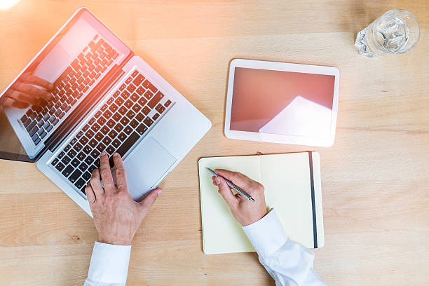 istock Cropped Hands Of Businessman Typing While Writing In Notepad On Desk At Office 691116647