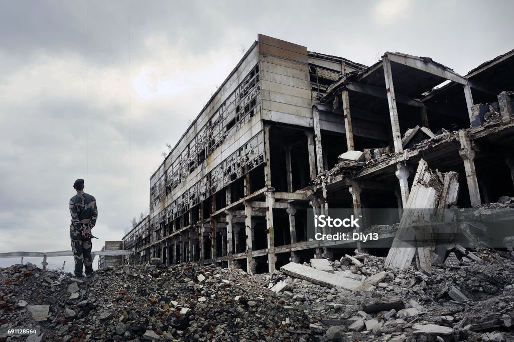 Soldier in military uniform stands on the ruins Soldier in military uniform stands on the ruins of the destroyed house. Hot spots on the planet. The concept of the fight against terrorism. Ukraine Stock Photo