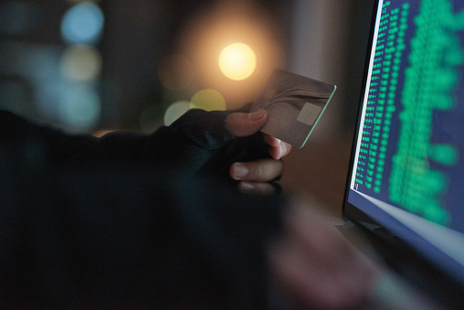 Shot of an unrecognisable hacker using a laptop to hack into a credit account