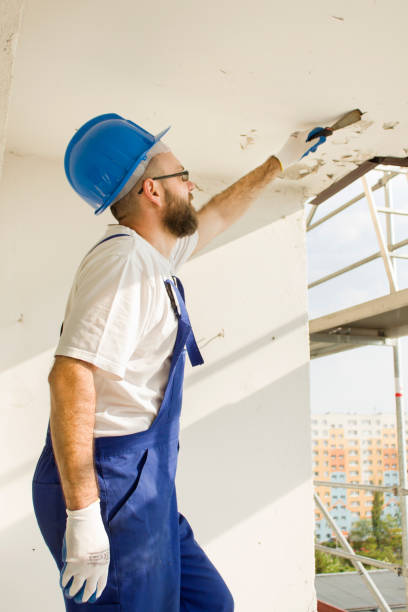 istock Construction worker in work attire, protective gloves and a helmet on site. Remove the old paint spatula from the ceiling. 691177594