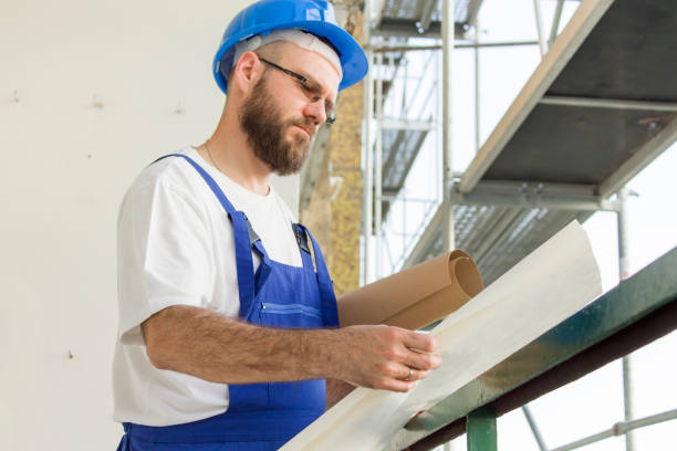 istock Construction worker in working outfit and in helmet stands at high altitude on construction site and inspects technical plans 691178080