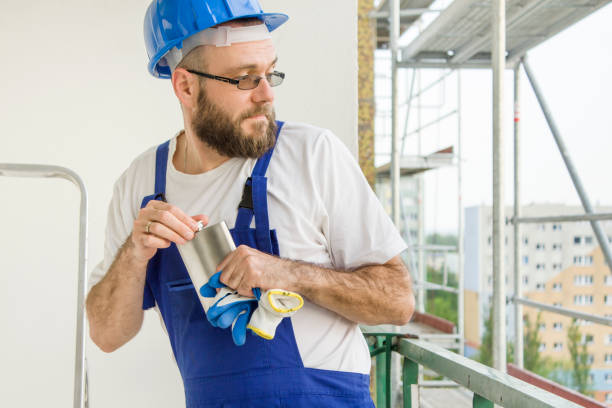 istock A construction worker in a work outfit, protective gloves and a helmet on his head pulls a silver hip-flask his pocket, looking back. Work at high altitude. Scaffolding in the background. 691178476
