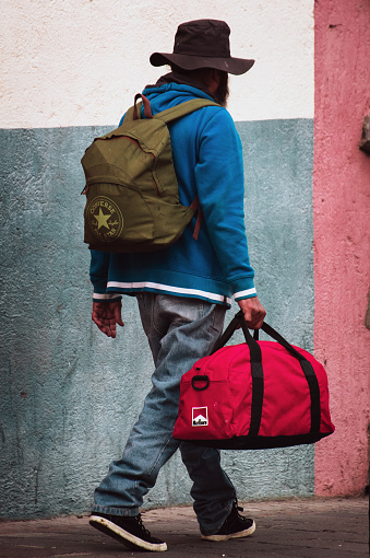 SANTA CRUZ, TENERIFE, SPAIN - DECEMBER 2016: Poor man with rucksack and red bag is walking along the street.