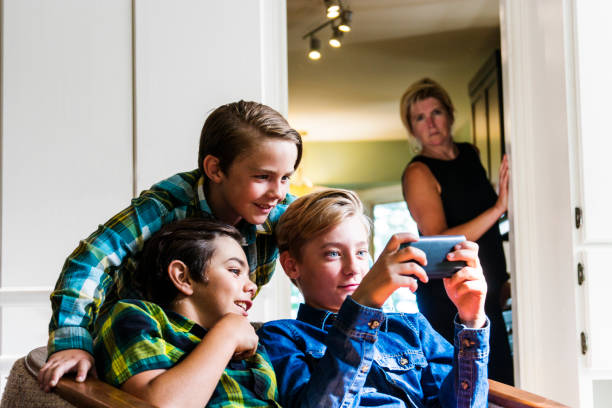 istock Mother with slightly concerned look on her face watching boys using the internet on a phone 691187238