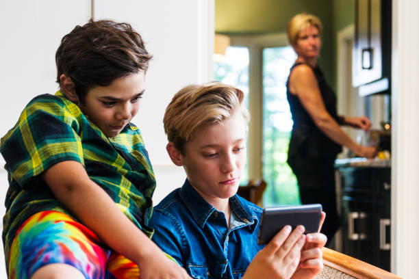 Mother with slightly concerned look on her face watching boys using the internet on a phone
