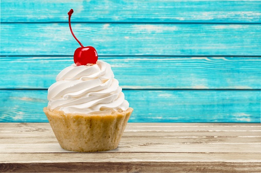 Cupcake with whipped cream and cherry isolated on background