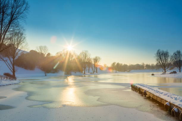 Strong winter that hit Europe freezes the Olympiasee at Olympia Park in Munich. Beautiful landscape in late afternoon when the sun falls over the park. The water of the small lake end the small pier are under severe cold weather.