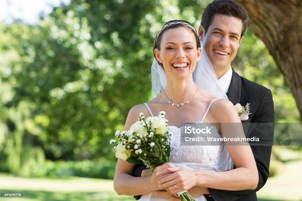 Newly wed couple with flower bouquet in park Portrait of newly wed couple with flower bouquet in park Wedding Stock Photo