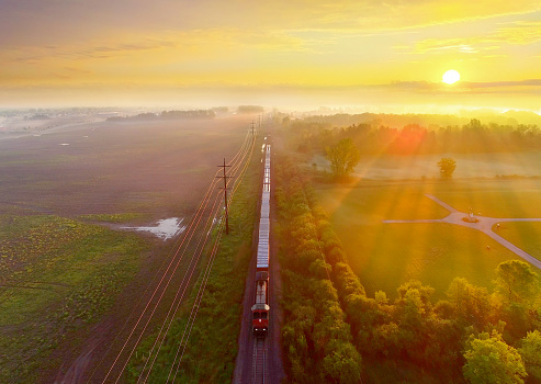 Train rolls through foggy rural landscape at sunrise, aerial view