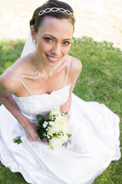 istock Bride holding flower bouquet while sitting on grass 691249326