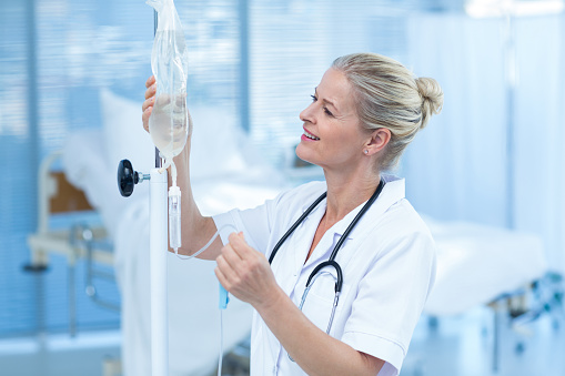 Nurse connecting an intravenous drip in hospital room