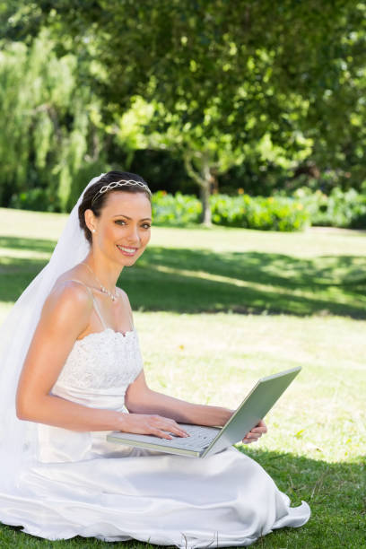 istock Beautiful bride with laptop sitting on grass 691273298