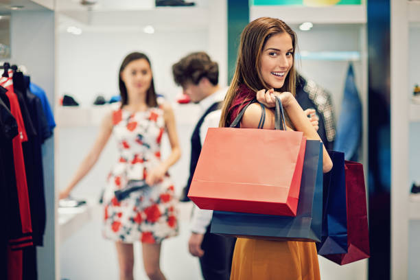 young beautiful girl is possing with her shopping bags in a boutique - reduction looking at camera finance business imagens e fotografias de stock