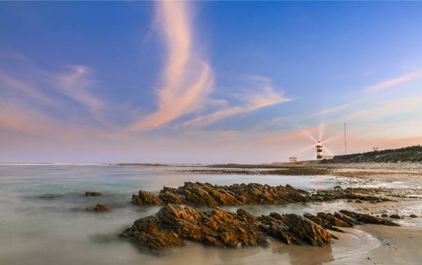 Lighthouse at dusk with rocks in the foreground stock photo