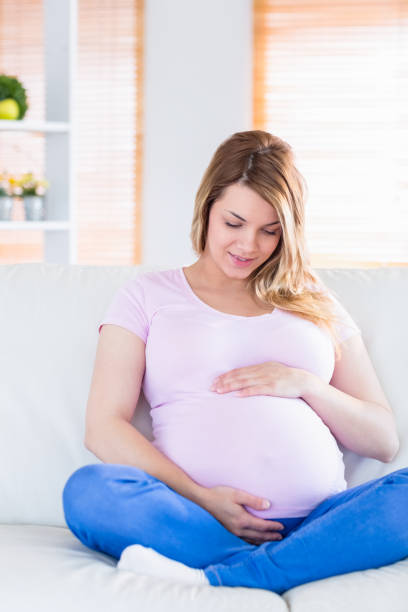 istock Pregnant woman sitting on couch touching her belly 691282942