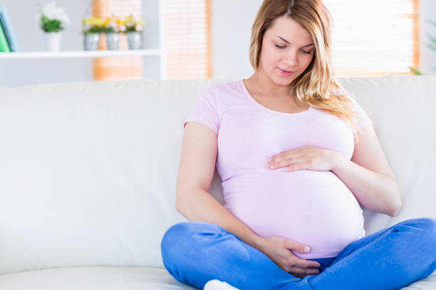 istock Pregnant woman sitting on couch touching her belly 691282948