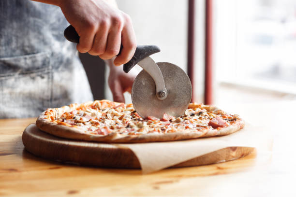 zbliżenie ręki szefa kuchni piekarza w jednolitym niebieskim fartuchu cięcia pizzy w kuchni - chef baker bakery flour zdjęcia i obrazy z banku zdjęć