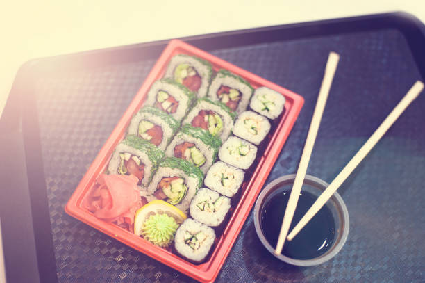 Japanese sushi in red plastic container for carrying food on black. Roll made of crab meat, avocado, cucumber inside and masago smelt roe outside. Top view of bento to-go plastic box, mixed nigiri and assorted sushi roll in lunch box place on wooden background. васаби stock pictures, royalty-free photos & images