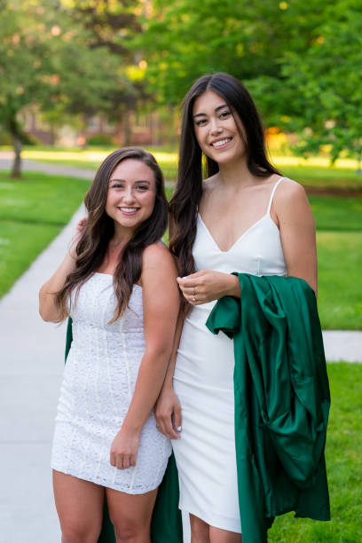 College Graduation Photo on University Campus Two college girls and best friends walk on a sidewalk while holding their caps and gowns before graduation on a university campus during the Spring in Oregon. sorority photos stock pictures, royalty-free photos & images