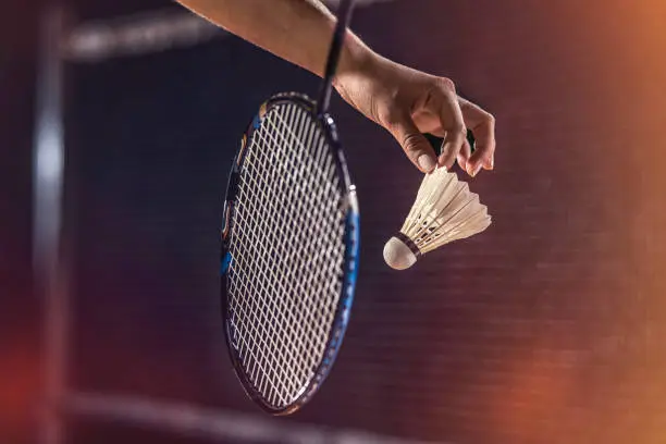 Close-up shot of a woman preparing to serve the shuttlecock near the net. Black background.