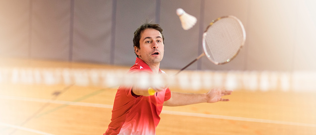 Panoramic photo of a man behind a net hitting a shuttlecock with his badminton racket.