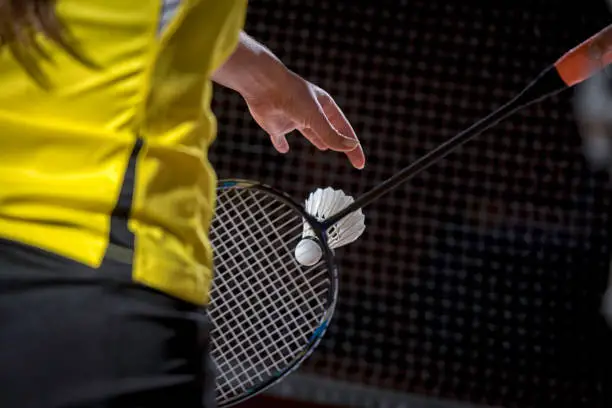 Woman holding a badminton racket and dropping a shuttlecock about to serve.