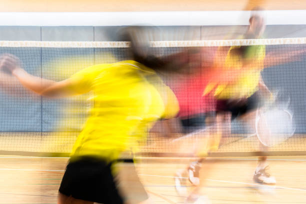 Rear view of there people playing badminton in an indoor court. Blurred motion.
