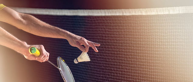 Close-up shot of a man’s hands, a badminton racket and a shuttlecock as he is preparing to serve.