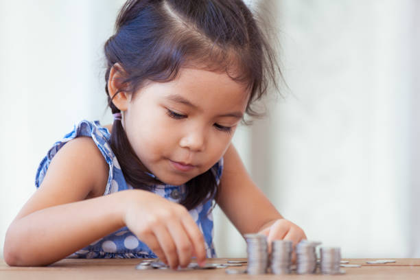 симпатичные азиатские маленькая девочка играет с монетами решений стеки денег - currency savings coin counting стоковые фото и изображения