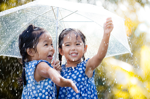 Two happy asian little girls with umbrella having fun to play with the rain together in vintage color tone