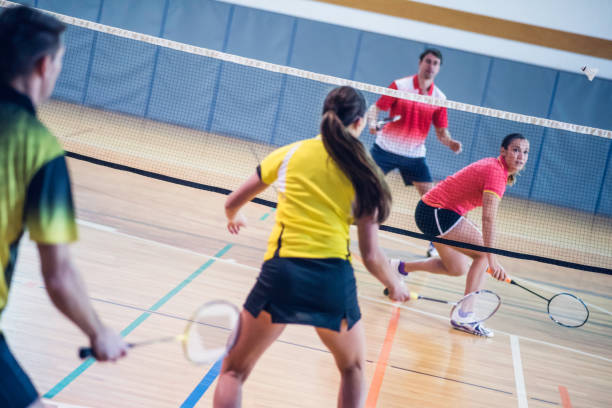 Two couples playing badminton Rear view of two couples playing badminton against each other on an indoor court. badminton stock pictures, royalty-free photos & images
