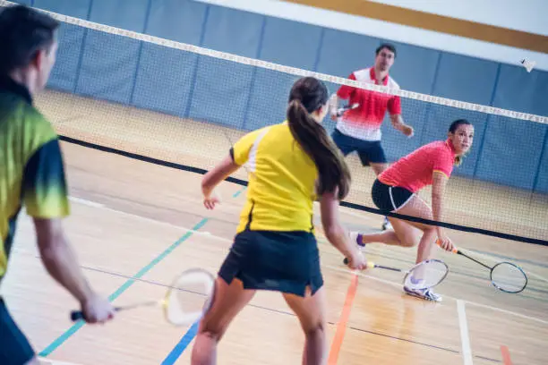 Rear view of two couples playing badminton against each other on an indoor court.