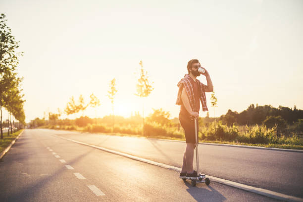Hipster drinking coffee on the bicycle trail and riding push scooter