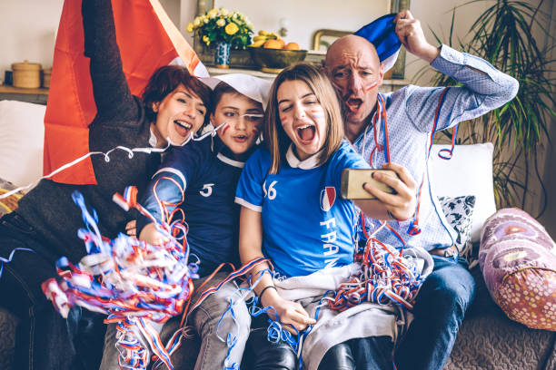 french cheering family watching soccer match on mobile on sofa french cheering family sitting on sofa watching soccer match on mobile at home with french flag french flag photos stock pictures, royalty-free photos & images