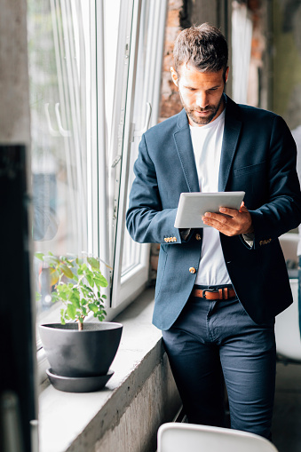 Businessman working in his modern office. Standing and typing on his digital tablet